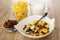 Bowl with dried grape, corn flakes in glass, pitcher with yogurt, spoon in bowl with raisin and corn flakes on table