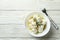 Bowl with feta cheese and fork on white wooden background