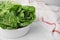 Bowl with fresh green romaine lettuces on white tiled table, closeup. Space for text