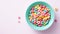 Bowl with fruit cereal rings on a light pink background, top view banner