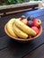 Bowl of fruit including bananas, apples and passion fruit on an outdoor wooden table