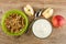 Bowl with granola, pieces of apple, spoon, bowl with yogurt on table. Top view