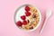 Bowl with greek yogurt, raspberries and muesli on pink table top view. Healthy diet breakfast