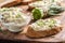 A bowl of homemade cream cheese spread with chopped chives surrounded by bread slices with spread and a bunch of freshly