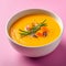 Bowl of homemade creamy pumpkin soup on a pink background