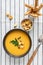 A bowl of homemade fresh spicy organic creamy pumpkin soup on a white striped textile background with bread sticks, sour cream,