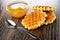 Bowl with honey, biscuit waffles, spoon on wooden table