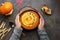 A bowl of hot pumpkin cream soup with sour cream and seeds in female hands in a woolen sweater on a dark rustic background. Autumn