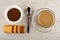 Bowl with instant coffee, teaspoon, cup of coffee with milk on saucer, cookies with filling on table. Top view