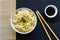 Bowl of instant cooked plain noodles with chopsticks and green a