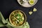 Bowl of linguine pasta with avocado sauce, green peas, zucchini, sprouts on dark grey table