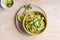 Bowl of linguine pasta with avocado sauce, green peas, zucchini, sprouts on rustic wood table