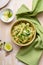 Bowl of linguine pasta with avocado sauce, green peas, zucchini, sprouts on rustic wood table