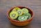 Bowl of many cut fresh kiwis on wooden table, closeup