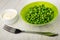 Bowl with mayonnaise, green bowl with cooked green peas, fork on table