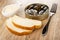 Bowl with mayonnaise, opened jar with sprats, slices of bread, fork on wooden table