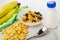 Bowl with muesli, heap corn flakes, bottle of yogurt, bananas