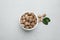 Bowl with nutmeg seeds and leaves on light table, flat lay