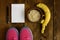 Bowl of oatmeal, Banana with yellow tape for measuring figure, empty notepad and trainers on dark wooden background