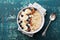 Bowl of oatmeal porridge with banana, blueberries, almonds, coconut and caramel sauce on teal rustic table, top view, flat lay