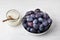 A bowl of plums and a jar of sugar, ingredients for making plum jam on a light gray background