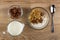 Bowl with porous chocolate, pitcher with yogurt, bowl with granola, yogurt, chocolate, spoon on table. Top view