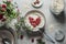 Bowl with porridge and heart shaped raspberries at grey concrete kitchen table with glass jar, branches, bowls and spoon.