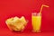 Bowl of potato chips and glass of orange drink in bright red background. Minimalistic image of attention grabbing snacks and