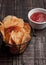 Bowl with potato crisps chips and ketchup on wooden board