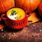 Bowl of pumpkin soup swirled with coconut cream with fresh pumpkins and bread crouton on wooden table.