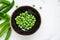 Bowl of raw green peas on a white rough background