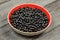 Bowl with red inside, full of blackcurrant, on wooden desk