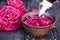 Bowl with red rose petals on a background of dark wooden boards and essential oil with roses