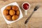 Bowl with round fried pies, sauceboat with ketchup, fork on table. Top view