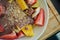 Bowl of sliced fruits and berries with chocolate souse and crushed walnuts standing on a wood board