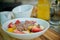 Bowl of sliced fruits and berries with chocolate souse and crushed walnuts standing on a wood board, orange juice