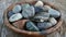 A bowl of smooth river stones sits on a wooden surface each one carefully selected for its healing properties. Some are