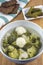 Bowl of soup with pieces of chicken, broccoli and cauliflower, bread and cucumbers on towel