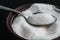 Bowl and a spoon full of white Sugar on black. Closeup