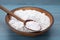 Bowl and spoon of natural starch on light blue wooden table, closeup