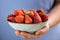 A bowl of strawberries held in one hand by a girl in pastel blue clothes