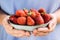 A bowl of strawberries held in two hands by a girl in pastel blue clothes