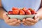 A bowl of strawberries held in two hands by a girl in pastel blue clothes