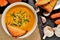 Bowl of sweet potatoes cream soup with fresh chive, roasted toast bread, pepper, carrot and garlic slate slab. Top view.