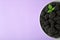 Bowl of tasty ripe blackberries  leaves on purple background, top view with space for text