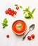 Bowl of tomato soup or gazpacho with spoon and basil on white wooden background