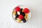 Bowl of yogurt with healthy fresh berries and granola, close up top view on white wood