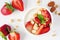 Bowl of yogurt with healthy strawberries and granola, close up above view on white wood