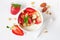 Bowl of yogurt with healthy strawberries and granola, close up top view on a white wood background