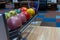 Bowling balls lie in a holder in a line. Colored balls and bowling